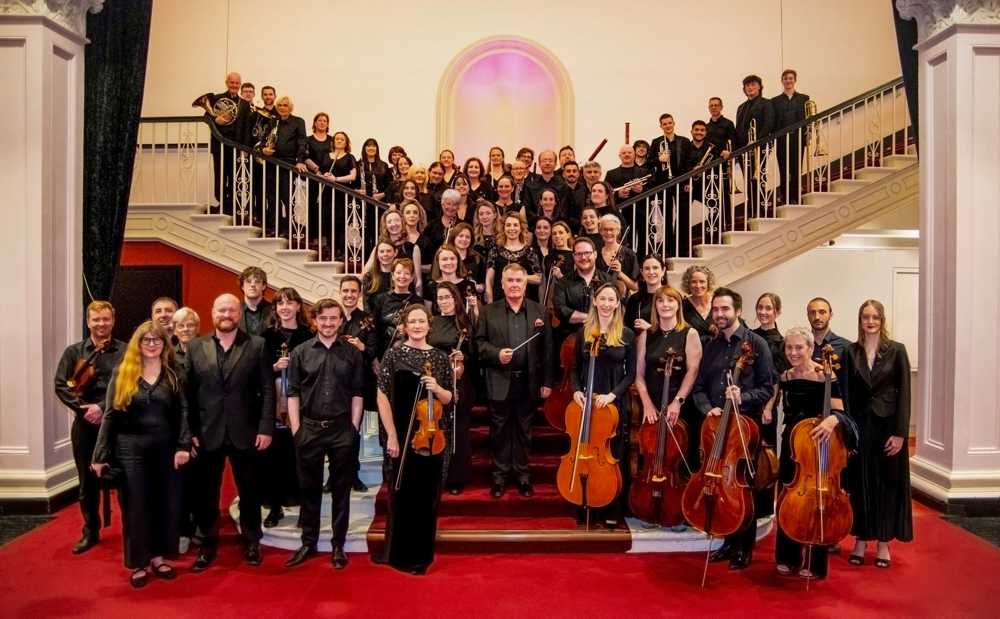 Hibernian Orchestra members posed on a grand staircase in formal concert attire