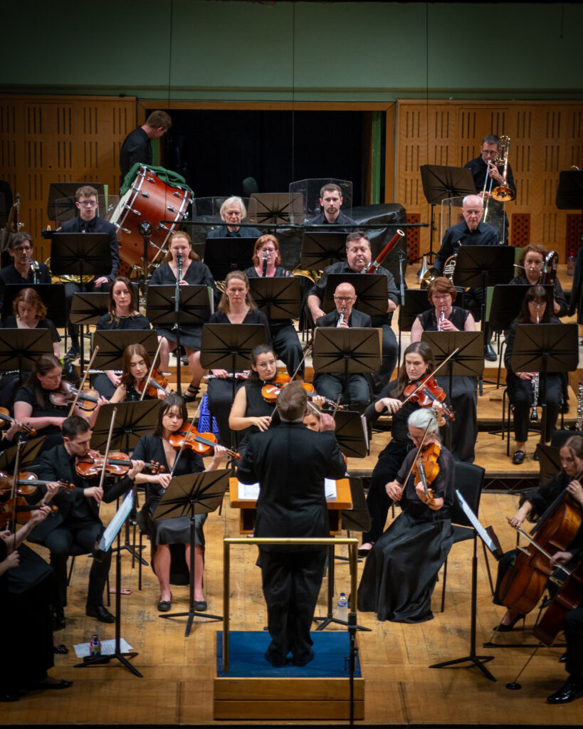 Hibernian Orchestra performing live on stage with conductor, string players, woodwind, brass, and percussion sections