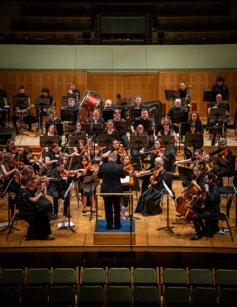 Hibernian Orchestra full orchestra performing live on stage with conductor, strings, woodwind, brass, and percussion sections in concert