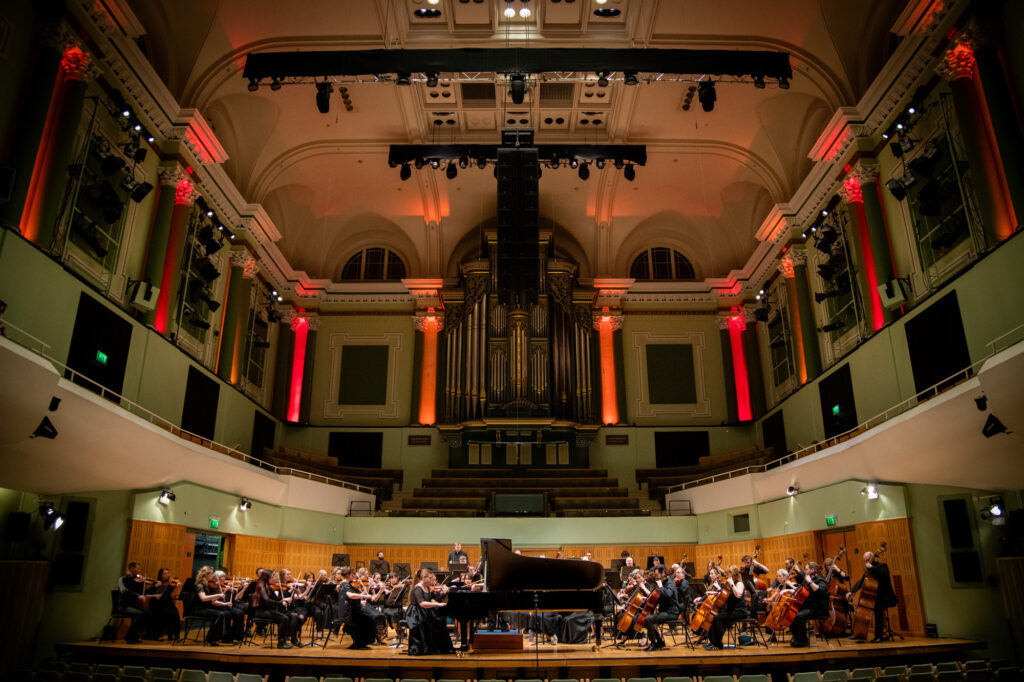 Hibernian Orchestra performing live on stage in a concert hall with warm red lighting